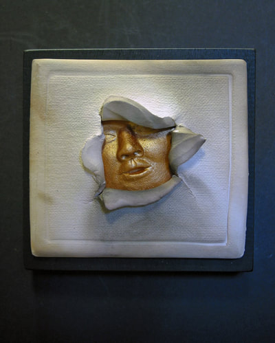 Small white pit fired ceramic piece mounted on 3.5" black wood. Gold face breaking out of center