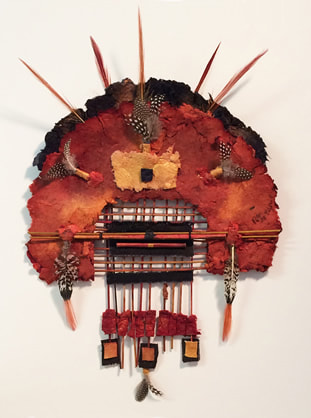 Handmade paper collage in the shape of a headdress with bamboo twigs and feathers. Predominately rust and black in color